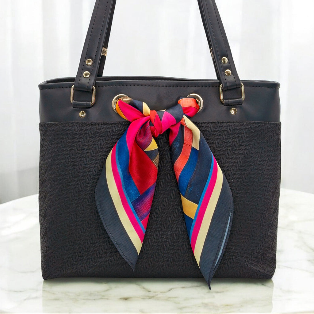 Black handbag with a colorful scarf tied around it on a white marble surface.